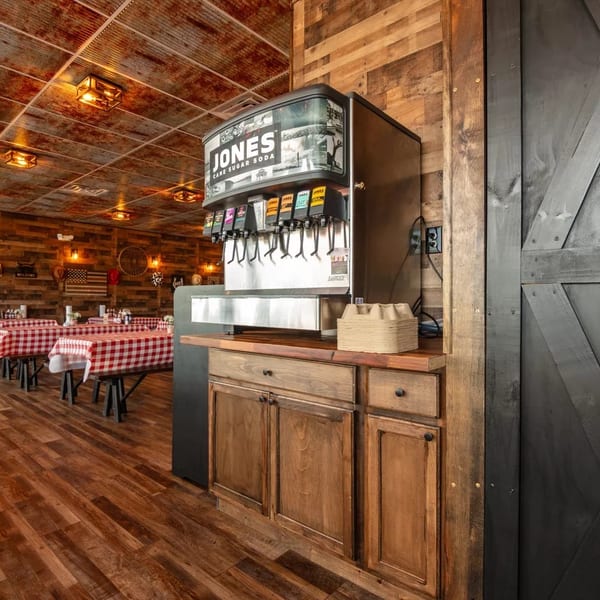 Rustic restaurant interior with a Jones Cane Sugar Soda machine, wooden walls, and red checkered tablecloths.