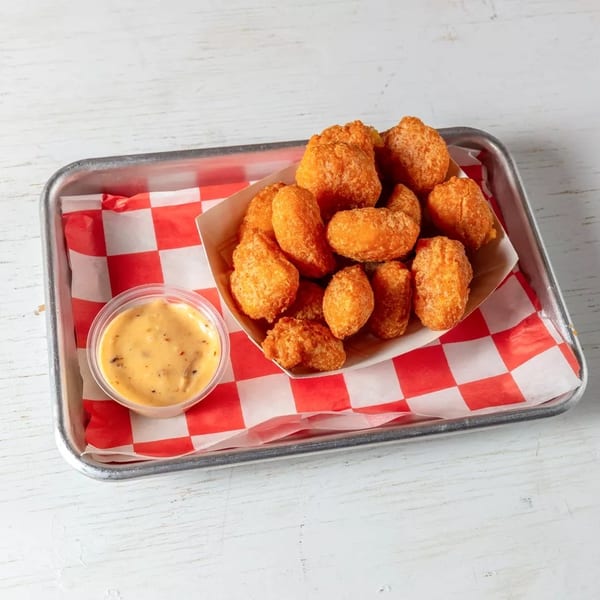 Golden fried tater tots in a paper tray with red and white checkered liner, served with dipping sauce.