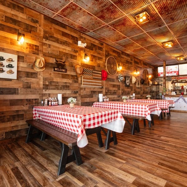 Rustic restaurant interior with wooden walls, red and white checkered tablecloths, and a service counter.