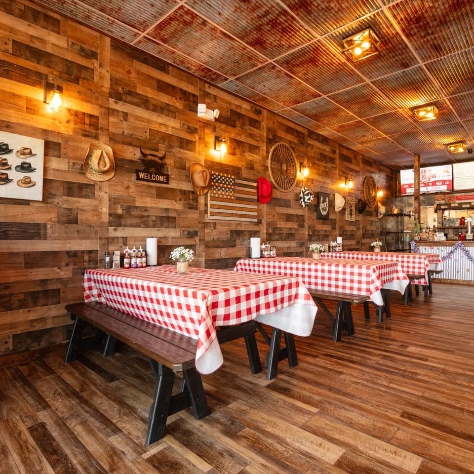 Rustic restaurant interior with wooden walls, red and white checkered tablecloths, and a service counter.