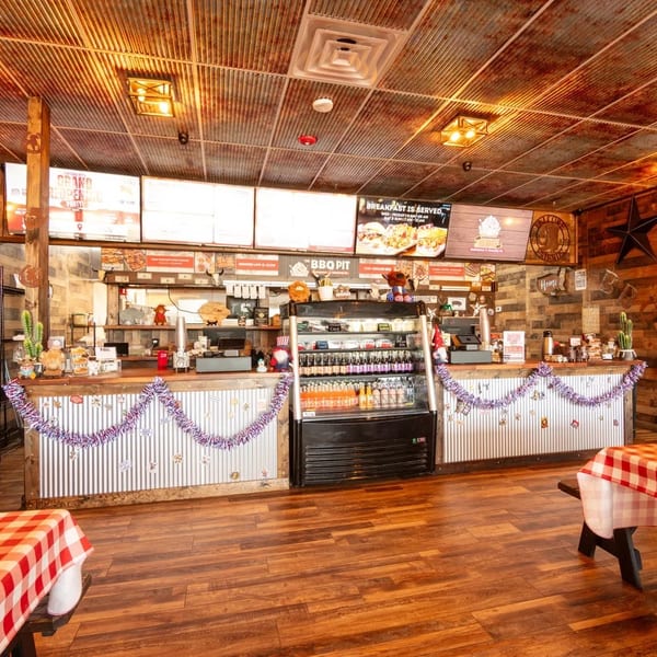 Rustic BBQ restaurant interior with corrugated metal and wood walls, decorated counter, and picnic tables.